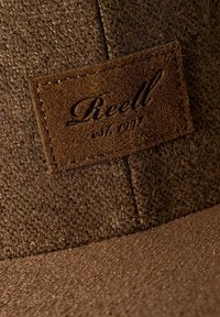 Brown cap made of textured fabric with a smooth visor; features a leather patch labeled "Reell" with established year 1997.