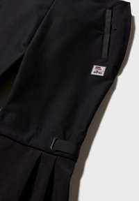 Schwarze Sporthose mit einem plissierten unteren Abschnitt, sicherem Bund mit Gürtelschlaufe und einem kleinen bestickten Logo in Grau, Rot und Blau.