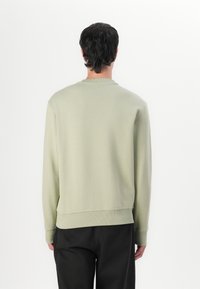 Sudadera verde claro hecha de tela suave. Con cuello redondo, puños acanalados y un dobladillo recto en la parte inferior. Diseño simple y minimalista.