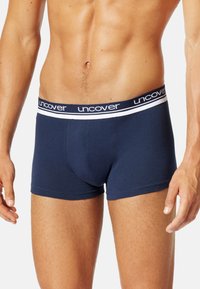 Marinblå boxershorts med en tajt passform, tillverkade av mjuk bomull, med ett vitt elastiskt midjeband med "uncover"-logotyp.
