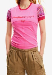 Rosa bomullströja med korta, flerfärgade stickade ärmar och ribbat halsband. Framsidan har ett grafiskt designelement som är diskret visat.