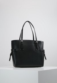 Zwarte leren tote bag met dubbele handvaten, een gladde textuur, zilveren hardware-accenten en een gestructureerde vorm. Zijvakjes voor extra functionaliteit.