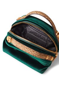 Sac à main en velours vert avec une poignée texturée en tan, quincaillerie dorée et doublure intérieure noire avec une étiquette de marque. Fermeture éclair en haut.