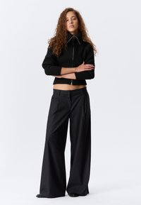 Czarny krótkie prążkowany sweter z wysokim kołnierzem i zamkiem błyskawicznym, zestawiony z luźnymi czarnymi spodniami w prążki. Gładka tekstura, dopasowany krój.