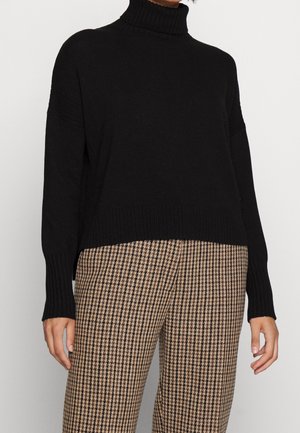 Pull en col roulé noir avec une texture côtelée, doté de manches oversize et d'un ourlet court, associé à un pantalon à motif pied-de-poule.