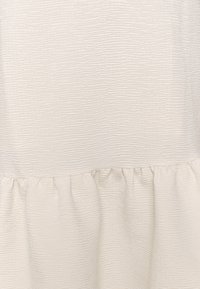 Krämfärgad tyg med subtila horisontella ribbade texturer och gathered sömdetalj nära nederkanten.