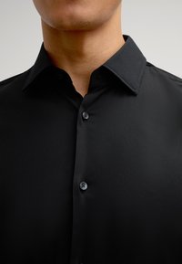 Zwarte button-up shirt met een klassieke kraag, gladde textuur en duurzame knopen, met een getailleerd ontwerp voor een moderne uitstraling.