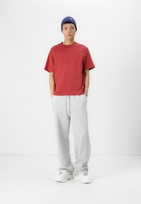 Tricou roșu cu mâneci scurte și croială lejeră, asortat cu pantaloni de trening gri deschis și adidași albi. Modelul poartă o căciulă tricotată bleu închis.