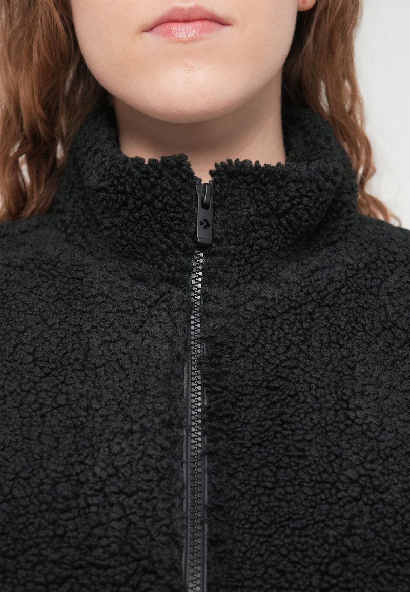 Sort fleecetrøje med høj krave og lynlås foran. Stoffet har en tekstureret, fluffy overflade, der skaber et hyggeligt udseende.