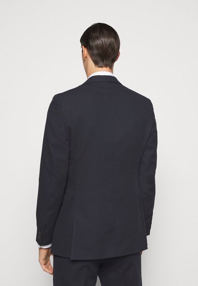 Blazer azul-marinho com um corte ajustado, fenda única e fecho de dois botões. Tecido suave com leve brilho e detalhes em bolsos laterais.