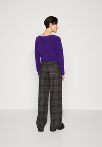 Pulover violet pufos cu spate decupat, asociat cu pantaloni cu picior larg din carouri în culorile negru, gri și bej, având buzunare la spate.