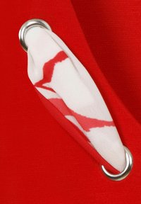 Roter Stoff mit strukturiertem Finish, der mit einem weißen und roten gemusterten Tuch durch ein silbernes Ösen-Detail gefädelt ist.