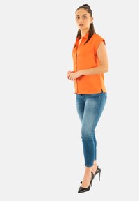 Camisa de botones naranja de manga corta combinada con jeans skinnys azul claro y zapatos de tacón negros. Tela suave, diseño ajustado.