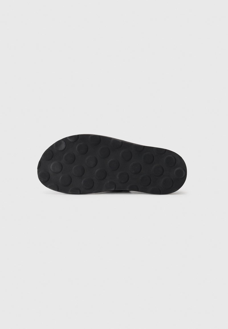 Black rubber sole featuring circular patterns for traction, with a smooth texture and rounded toe shape.