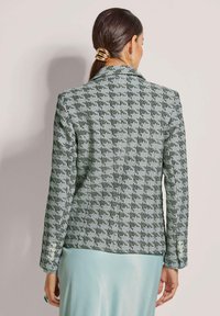 Grüner und weißer kariertes Blazer mit Reverskragen, langen Ärmeln und Knopfdetails, kombiniert mit einem hellblauen Rock.