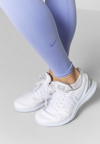 Světle fialové legíny s jemným logem Nike a bílé tenisky se šedými detaily a modrými podrážkami. Materiál legín je hladký a dobře přiléhá.