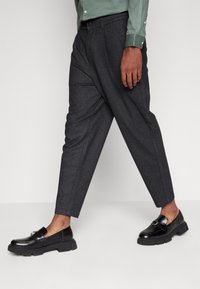 Grå skräddarsydda byxor med en avsmalnande design, tillverkade av ett texturerat tyg, i kombination med eleganta svarta loafers med en dekorativ hårdvaruaccent.