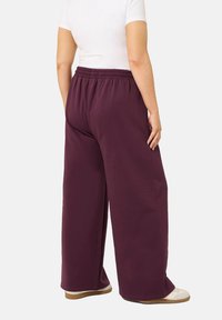 Hellebeine in dunkelburgunderfarbener Stoff mit einem elastischen Bund. Das Material scheint weich und mit einer glatten Oberfläche zu sein.