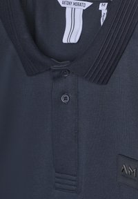 Polo navy con colletto a costine, due bottoni neri e tessuto strutturato. Presenta un piccolo etichetta nera con "AM."