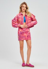 Roze tie-dye denim jack en bijpassende rok, gecombineerd met een blauwe crop top. Roze suede schoenen maken de look compleet. Soepele textuur, cropped ontwerp.