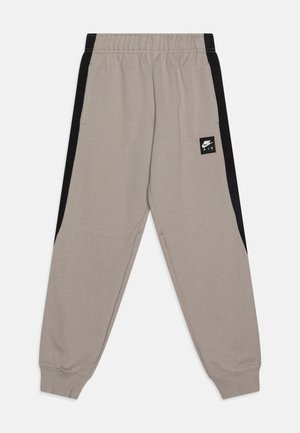 Beżowe spodnie dresowe Nike Air z czarnymi bocznymi panelami, elastycznym pasem, ściągaczami przy kostkach oraz małą naszywką z logo Nike na lewej udzie.