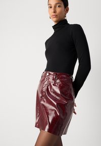 Bordeaux-farbenen Leder-Minirock, hoch geschnitten mit glänzender Textur, kombiniert mit einem enganliegenden schwarzen Rollkragenpullover, nahtlosem Design und seitlichen Taschen.