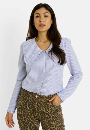 Blouse rayée bleu clair et blanche avec un col volanté et des boutons, associée à un pantalon en imprimé léopard brun. Manches longues avec des poignets volantés.