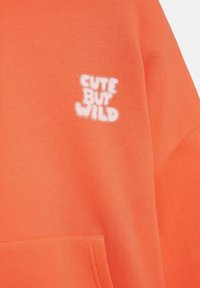 Bright orange sweatshirt featuring a white embroidered logo "CUTE BUT WILD" on the front; soft texture with a relaxed fit and kangaroo pocket.