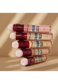 Cinque correttori multiuso con tubi cilindrici in plastica trasparente. Ognuno ha un applicatore arrotondato e morbido con etichette colorate che indicano i numeri delle tonalità.
