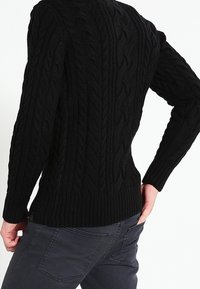 Pull noir en maille torsadée avec ourlet et poignets côtelés, présentant un motif texturé sur le corps. Le dos est montré avec une coupe ajustée.