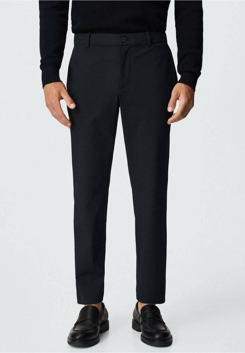 Černé kalhoty na míru, ve slim střihu, vyrobené z hladké látky. Mají zapínání na knoflík a boční kapsy, doplněné černými mokasíny.