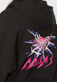 Czarna bluza z kapturem z kolorową grafiką na plecach, z motywem rozbłysku gwiazdy, różowymi i niebieskimi akcentami oraz logo w pogrubionych literach.