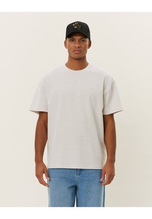 Grey cotton T-shirt with short sleeves, round neckline, and relaxed fit, paired with light blue denim jeans and a black cap featuring floral embroidery.