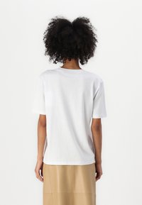 Balta kokvilnas T-kreklis ar īsām piedurknēm, apaļu kakla izgriezumu un brīvu piegriezumu. Gluda tekstūra un sānu slēgumi komfortam.