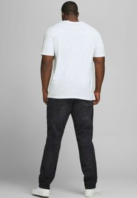 Weiße Kurzarm-T-Shirt kombiniert mit dunkelblauen Jeans. Das Outfit wird mit weißen Sneakers abgerundet, gesehen von hinten.