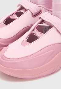 Κοντινό πλάνο ροζ slip-on sneakers με χοντρές σόλες, ευρείς ελαστικές λωρίδες και λεπτομέρειες από σατέν κορδέλα.