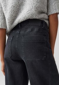 Jeans in denim nero con vita aderente e due tasche posteriori, caratterizzati da una texture leggermente sbiadita. Il tessuto appare resistente e liscio.