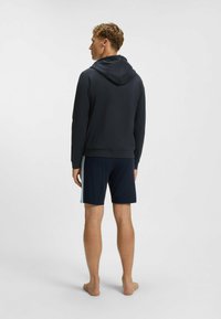 Navy hoodie gemaakt van zachte stof, met een relaxte pasvorm. Gepaard met donkere shorts, die een minimalistisch ontwerp laten zien.
