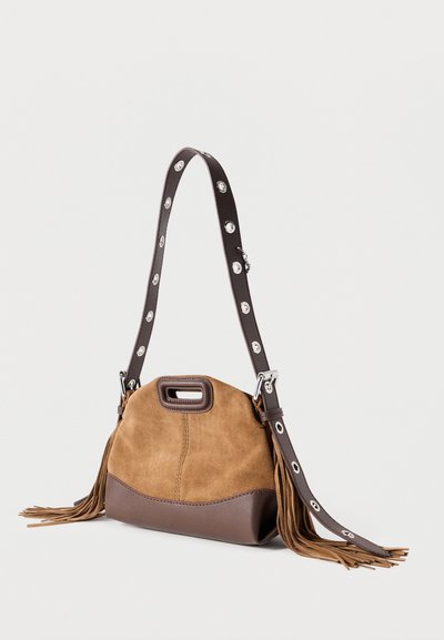 Καφέ σουέτ τσάντα με στρογγυλεμένο σχήμα, διαθέτοντας βάση από σκούρο καφέ δέρμα. Ο ιμάντας έχει ασημένια μεταλλικά στοιχεία και διακοσμητικές φούντες.