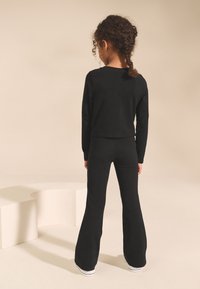 Melns garroku īsais tops un izplatītas bikses no mīksta auduma. Piedāvā brīvu piegulumu ar gludu tekstūru un vienkāršu dizainu.