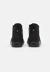 Zwarte gebreide enkelboots met een gestructureerd ontwerp, gecamoufleerde rubberen zolen en een kleine groene steraccent aan de achterkant.