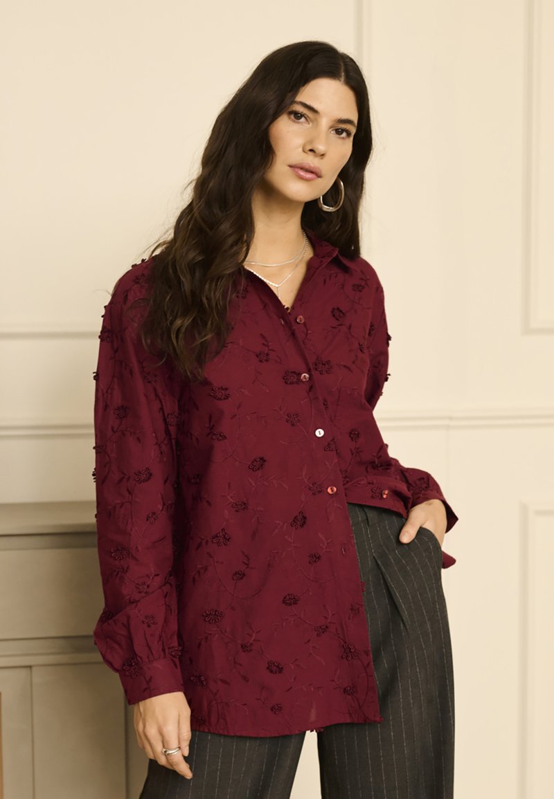 Bordeaux broderet skjorte med lange ærmer og blomster mønster. Kombineret med stribede bukser, hvilket skaber et lagdelt look.