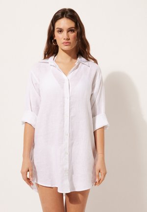 Witte linnen blouse met een ontspannen pasvorm, voorzien van een knoopsluiting aan de voorkant, opgerolde mouwen en een puntige kraag. Soepele textuur en lichtgewicht ontwerp.