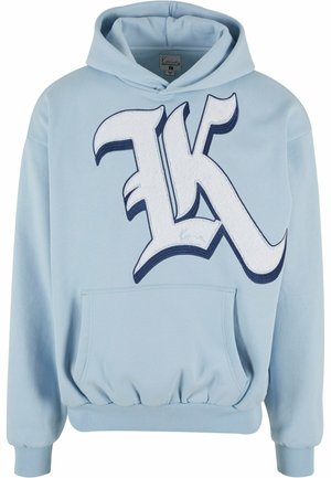Light blue hoodie with a large white and navy embroidered “K” logo, kangaroo pocket, ribbed cuffs, and waistband. Soft fabric texture.