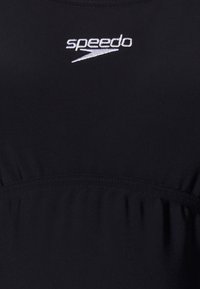 Svart Speedo-badkostym i slätt tyg; har gathered-detaljer vid midjan och en vit logotyp vid bröstet.