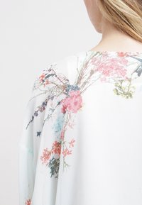 Bluse mit Blumenmuster in Pastellfarben, aus einem leichten, transparenten Stoff, mit lockerem Schnitt und weiter Halslinie. Akzente sind bunte Blumenmuster.