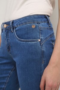 Jean en denim bleu avec une coupe ajustée, présentant des finitions en cuivre, des accents cousus et une texture lisse. Poches avant et arrière comprises.