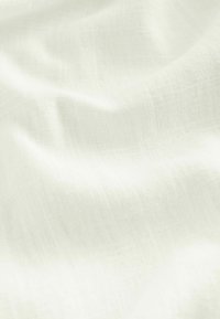 Könnyű, gyűrött fehér szövet, átlátszó textúrával; finom szőtt mintákkal és lágy fényláttal rendelkezik.