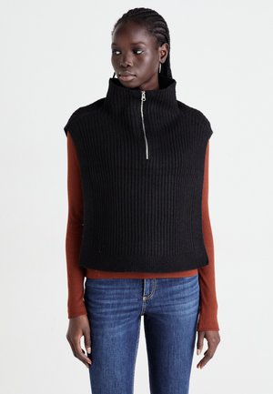 Black ribbed knit sleeveless top with high collar and zip closure, paired with a rust long-sleeve shirt and blue jeans. Smooth texture.
