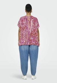 Short-sleeve blouse with a multicolored paisley pattern in pink and purple tones. Loose fit with a back keyhole detail. Paired with light blue baggy jeans.